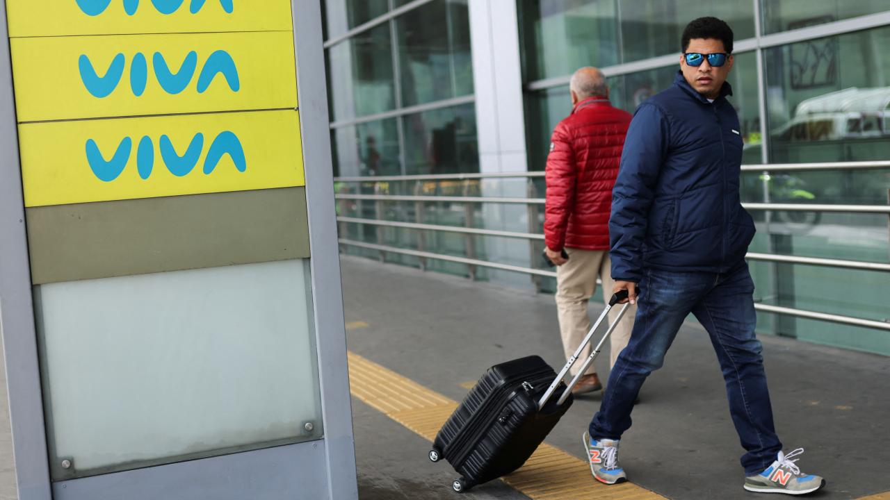 Hombre caminando con una maleta ceraca a cartel de Viva Air.