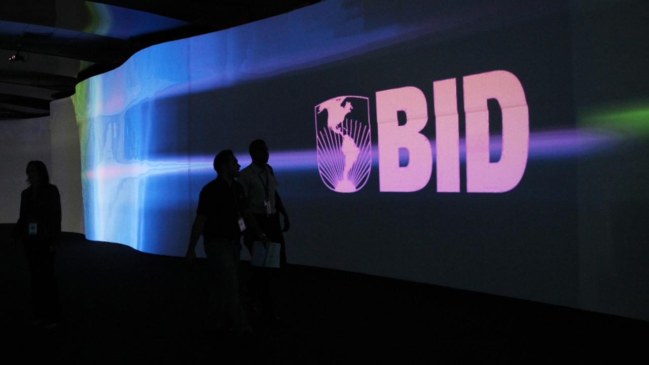 Visitantes caminan frente a una pantalla con el logo del Banco Interamericano de Desarrollo (BID) en el Centro de Convenciones Atlapa en Ciudad de Panamá.