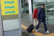 Hombre caminando con una maleta ceraca a cartel de Viva Air.